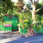 Mange steder blev der leget med alternative materialer til blomsterkasser, blomsterkummer og rumdelere. Her er det farvede mælkekasser eller lignende der er brugt. Ganske dekorativt syntes jeg.